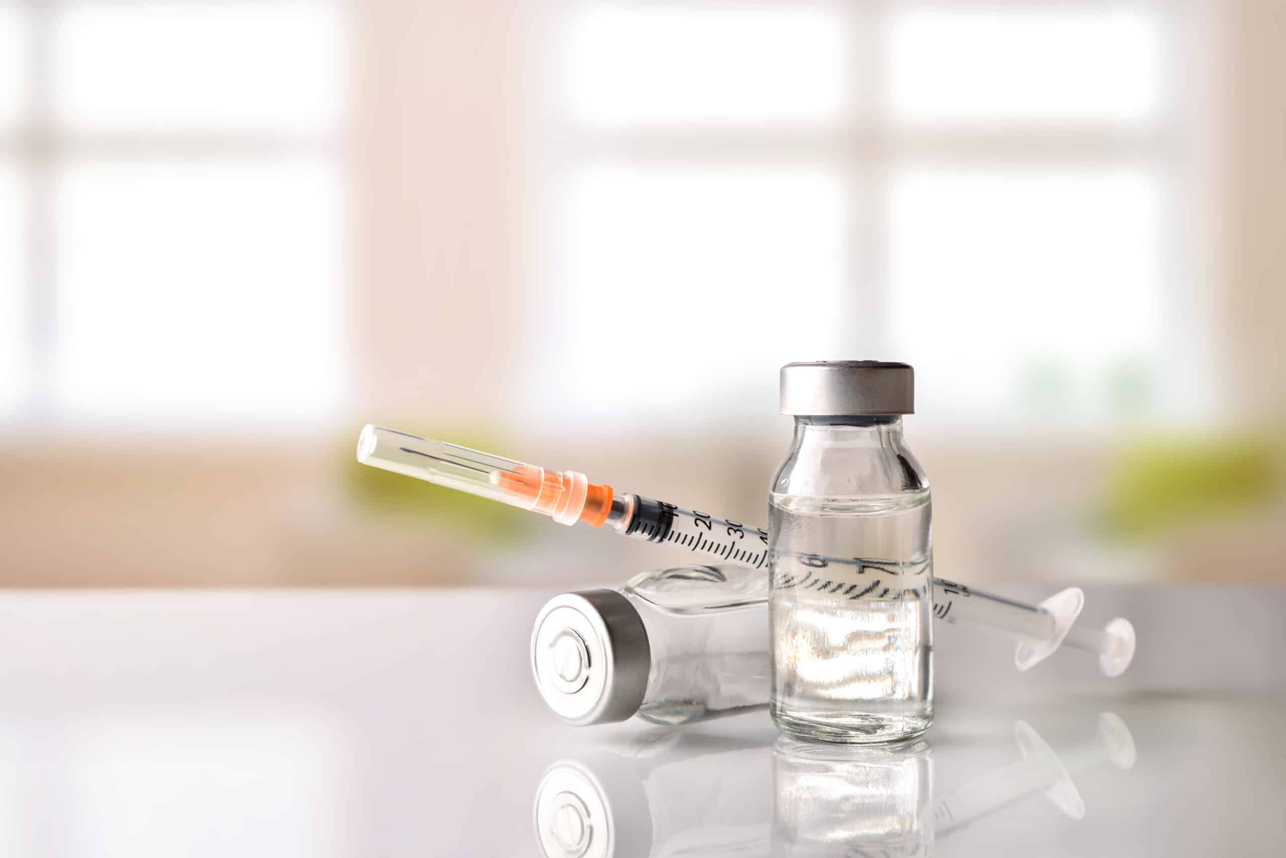 A vial and syringes on a clinical surface ready for injection, suggesting a sterile medical setting.